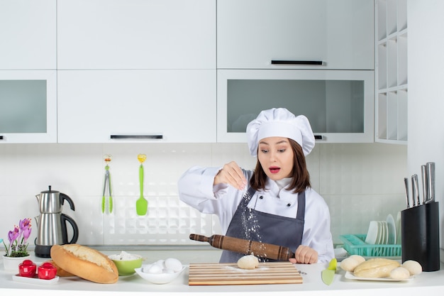 Jonge drukke vrouwelijke chef-kok in uniform die achter tafel staat en gebak bereidt in de witte keuken