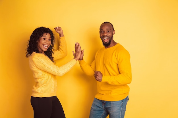 Jonge emotionele afro-amerikaanse man en vrouw in lichte vrijetijdskleding die zich voordeed op gele achtergrond. mooi koppel. concept van menselijke emoties, gezichtsuitdrukkingen, relaties, advertentie. teamwerk.