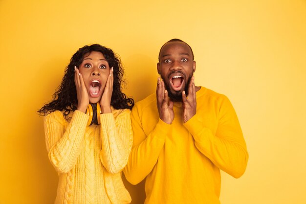 Jonge emotionele Afro-Amerikaanse man en vrouw in lichte vrijetijdskleding op gele achtergrond. Mooi paar. Concept van menselijke emoties, gezichtsuitdrukking, relaties. Verbaasd, verwonderd, geschokt.