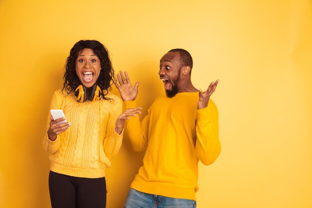 Jonge emotionele Afro-Amerikaanse man en vrouw in lichte vrijetijdskleding op gele ruimte. Mooi paar