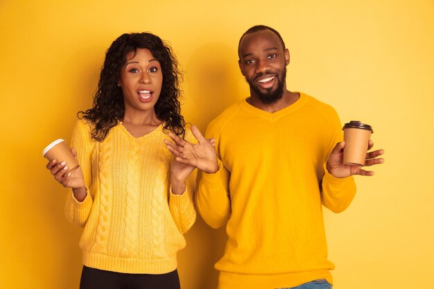 Jonge emotionele Afro-Amerikaanse man en vrouw in lichte vrijetijdskleding op gele ruimte