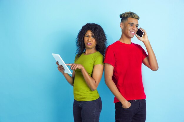 Jonge emotionele man en vrouw in kleurrijke kleding op blauw.