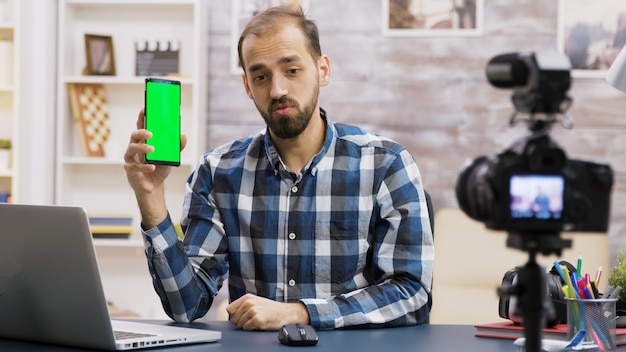 Jonge en beroemde influencer filmt een recensie van een telefoon met groen scherm. Creatieve contentmaker.