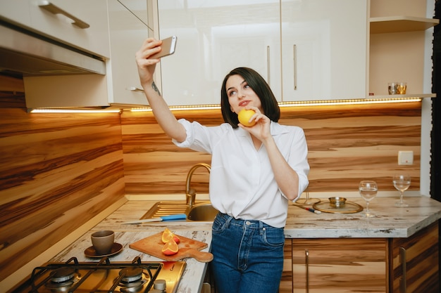 Jonge en mooie brunette staan ​​in de keuken met telefoon