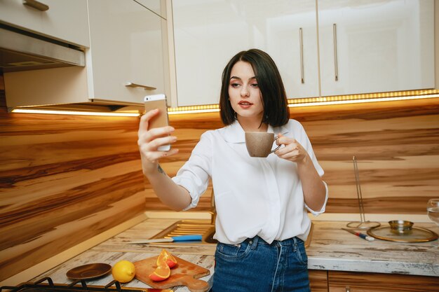 jonge en mooie brunette staan ​​in de keuken met telefoon