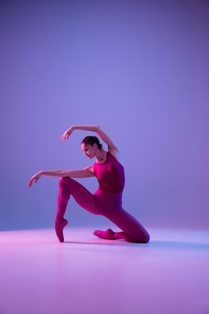 Jonge en sierlijke balletdanser geïsoleerd op paarse studio achtergrond in neonlicht