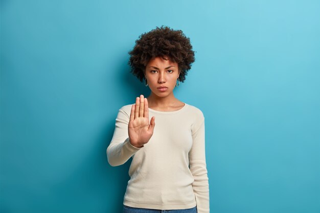 Jonge ernstige donkerhuidige vrouw toont het verbodssymbool van het stopbord houdt de handpalm naar voren