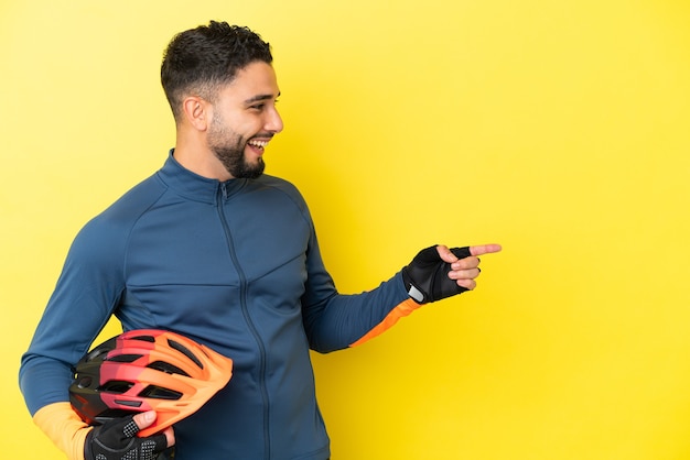 Jonge fietser arabische man geïsoleerd op gele achtergrond wijzende vinger naar de zijkant en presenteren van een product