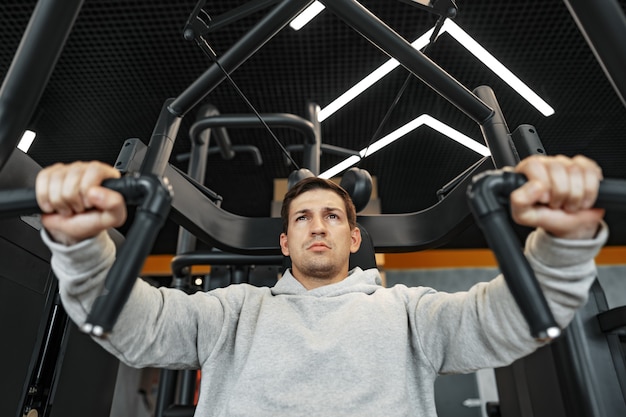 Jonge fit bodybuilder man doet armen training training in de sportschool op machine