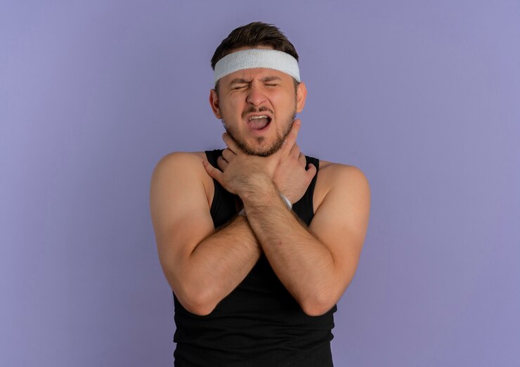Gratis Foto jonge fitness man met hoofdband zijn nek aanraken die lijdt aan pijn die zich over paarse muur bevindt