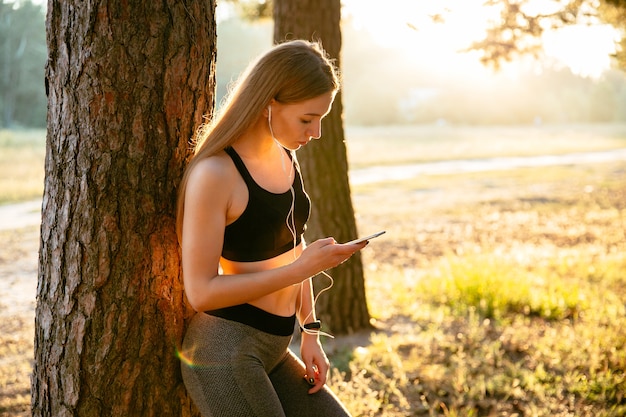 jonge fitness meisje, luisteren naar muziek in oortelefoons en het gebruik van een smartphone