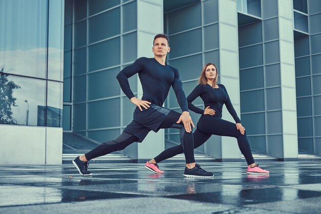 Jonge fitness paar in een sportkleding, een lunges doen in de moderne stad tegen een wolkenkrabber. Gezond levensstijlconcept.