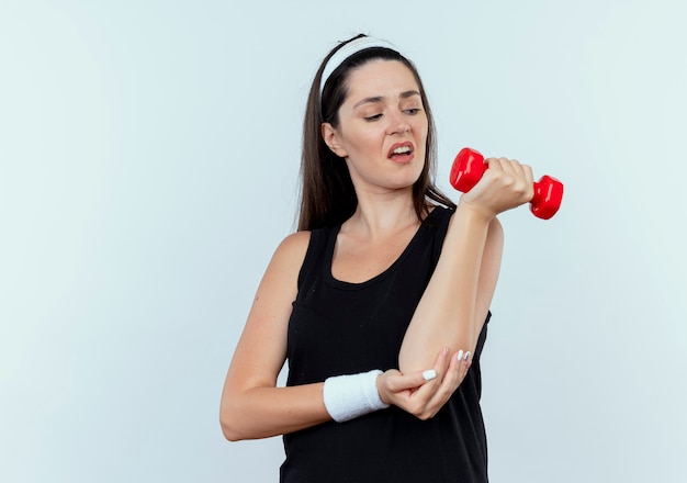 Jonge fitness vrouw in hoofdband uit te werken met halter op zoek gespannen staande op witte achtergrond