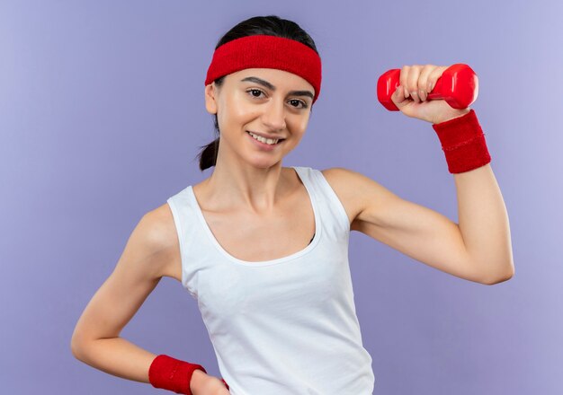 Jonge fitness vrouw in sportkleding halter poseren voor camera opheffen vuist glimlachend vrolijk staande over paarse muur