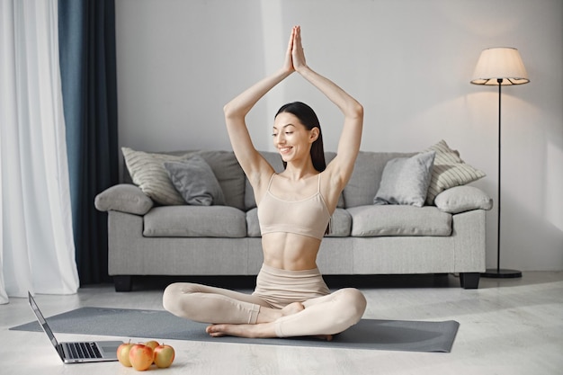 Jonge fitnessvrouw die thuis op een yogamat zit en een laptop gebruikt