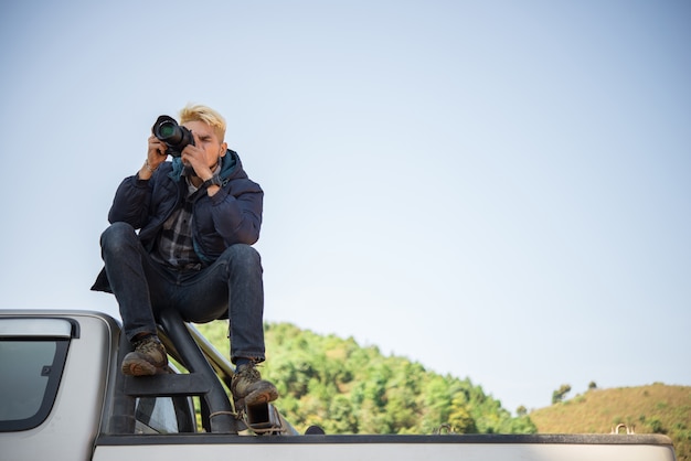 Jonge fotograaf zittend op zijn pick-up truck fotograferen in de berg.