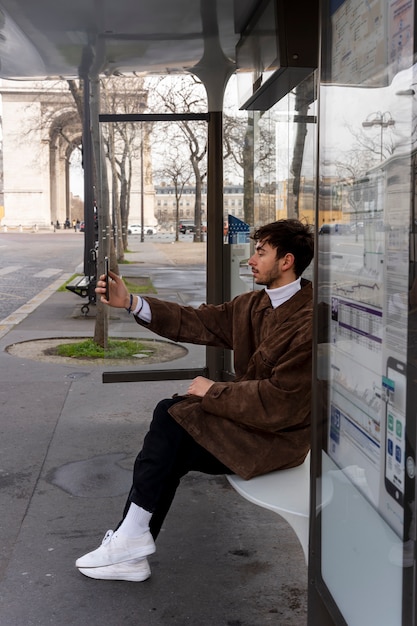 Gratis foto jonge franse man wacht op het station op de bus en neemt selfie