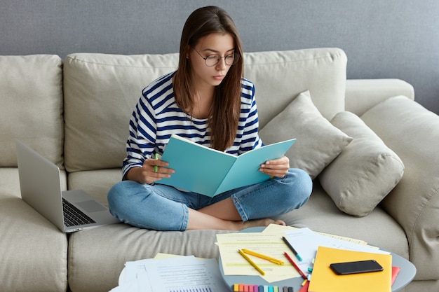 Jonge freelancer doet ditance werk thuis, studeert, zit gekruiste benen op de bank