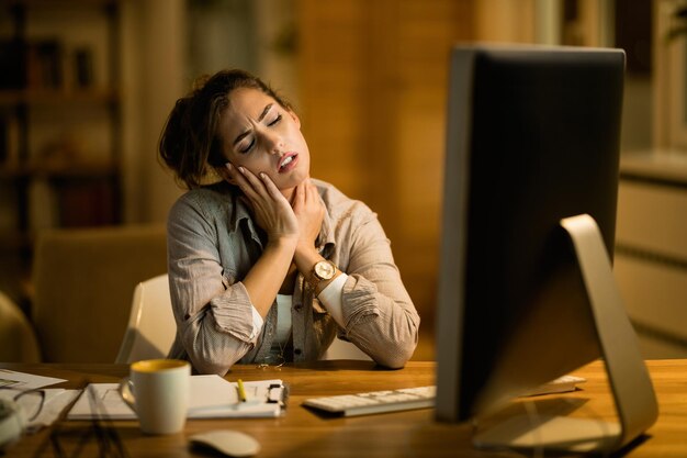 Jonge freelancer voelt pijn in haar nek terwijl ze laat op een computer werkt