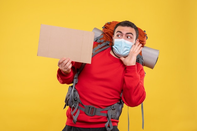 Jonge gefocuste reiziger die een medisch masker met rugzak draagt en een laken vasthoudt zonder op geel te schrijven