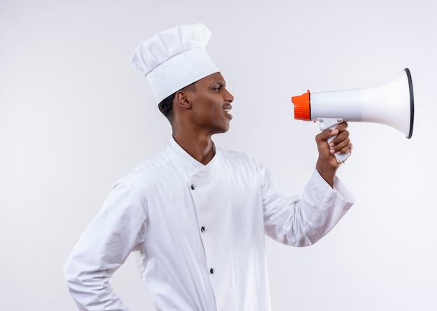 Jonge geïrriteerde Afro-Amerikaanse kok in uniform chef houdt luidspreker geïsoleerd op een witte achtergrond met kopie ruimte