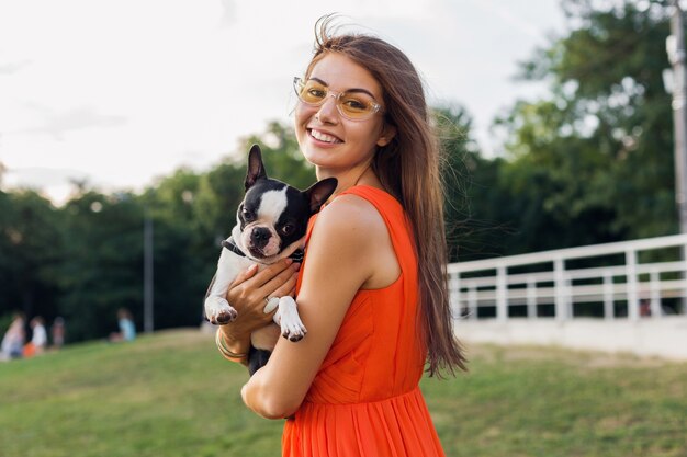 Jonge gelukkig lachende vrouw in oranje jurk plezier spelen met hond in park, zomer stijl, vrolijke sfeer
