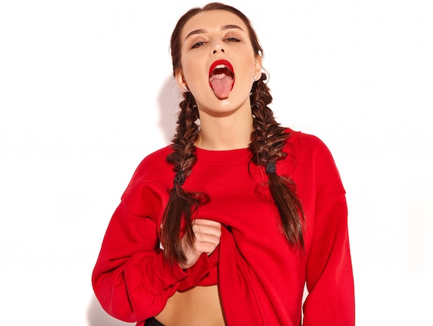 jonge gelukkig lachende vrouw model met lichte make-up en kleurrijke lippen met twee pigtails en zonnebril in zomer rode kleding geïsoleerd. toont haar tong