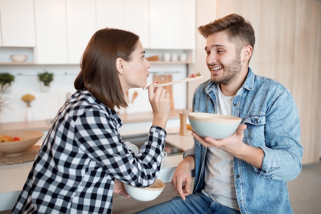 Jonge gelukkig man en vrouw in de keuken, eten ontbijt, paar samen in de ochtend, glimlachend