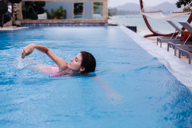 Jonge gelukkige fit slanke Europese vrouw in helder roze bikini blauw zwembad