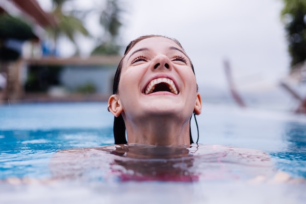 Jonge gelukkige fit slanke Europese vrouw in helder roze bikini blauw zwembad