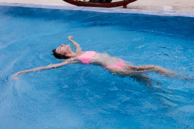 Jonge gelukkige fit slanke Europese vrouw in helder roze bikini blauw zwembad