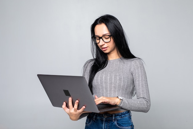 Jonge gelukkige glimlachende vrouw die in vrijetijdskleding laptop houden die op grijze muur wordt geïsoleerd