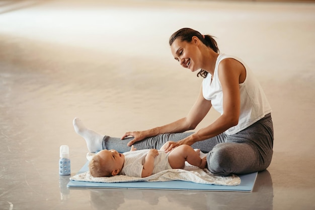 Jonge gelukkige moeder die haar benen strekt en plezier heeft met haar babyjongen tijdens het sporten in de gezondheidsclub