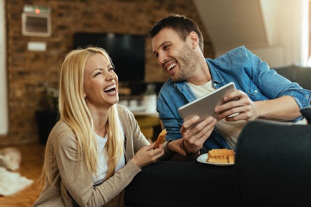 Jonge gelukkige paar lachen tijdens het kijken naar iets grappigs op touchpad thuis.