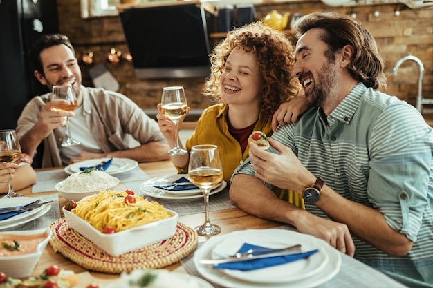 Jonge gelukkige paar praten over iets grappigs en lachen terwijl ze lunchen met hun vrienden thuis