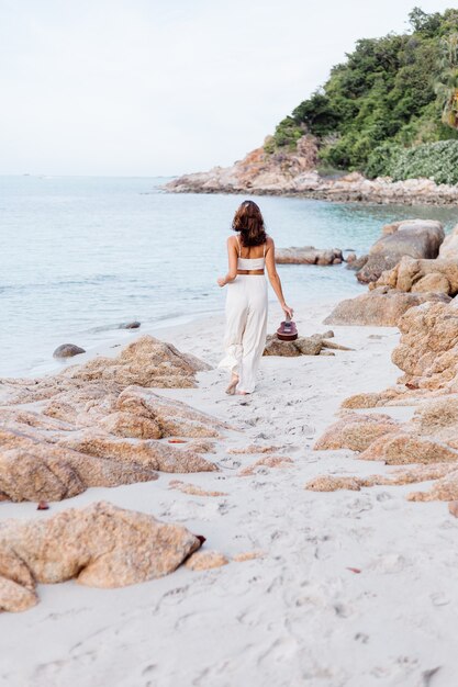 jonge gelukkige rustige blanke vrouw met ukelele op tropisch rotsachtig strand bij zonsondergang