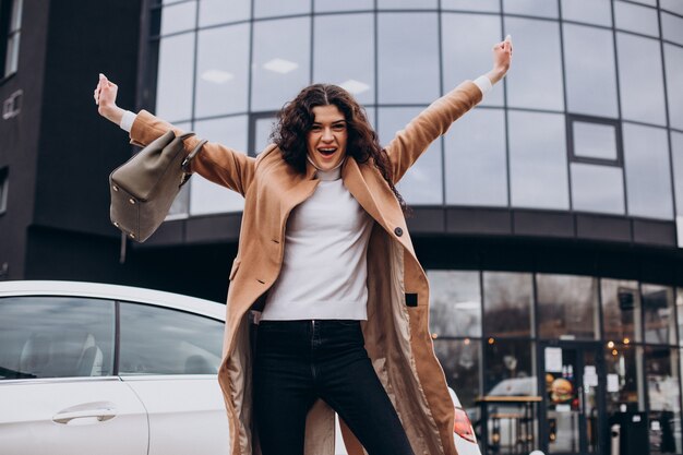 Jonge gelukkige vrouw die bij de auto staat