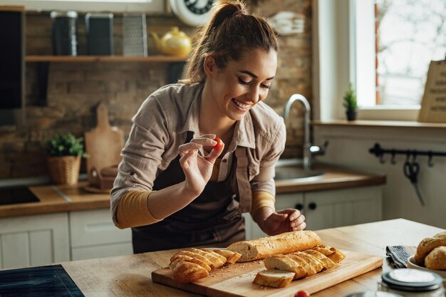 Jonge gelukkige vrouw die bruschetta maakt tijdens het bereiden van voedsel in de keuken