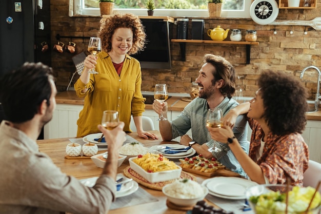 Jonge gelukkige vrouw die een toast voorstelt terwijl ze thuis luncht met haar duivels