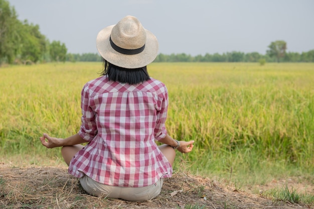 Jonge gelukkige vrouw die geniet van en mediteert met het mooie uitzicht op het rijstterras in Azië, Thailand. Reisfoto. Levensstijl. vrouw zit op rijstveld buiten het beoefenen van yoga ontspanning.