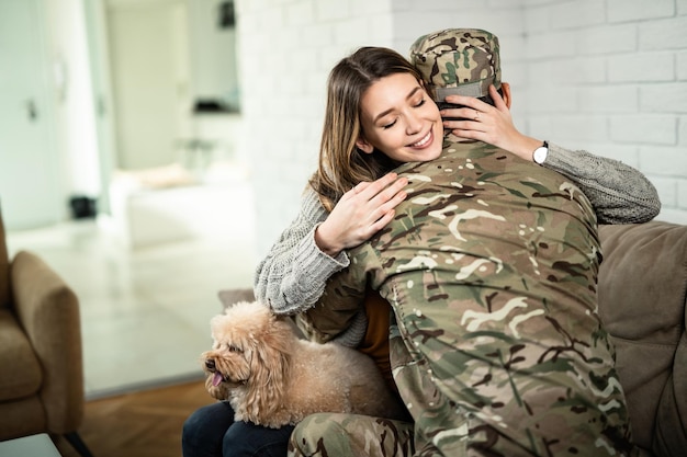 Jonge gelukkige vrouw die haar militaire echtgenoot omhelst die uit de oorlog thuiskwam