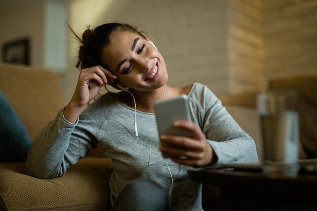 Jonge gelukkige vrouw die 's avonds geniet tijdens het gebruik van een smartphone in de woonkamer