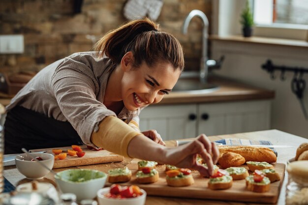 Jonge gelukkige vrouw genieten tijdens het maken van bruschetta in de keuken.
