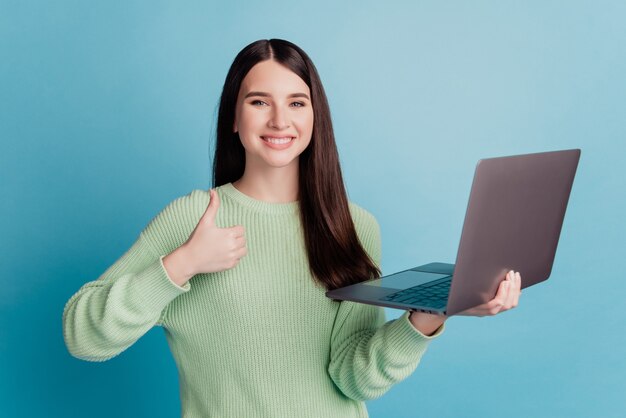 Jonge gelukkige vrouw met laptop toont thumbup teken geïsoleerd op blauwe achtergrond