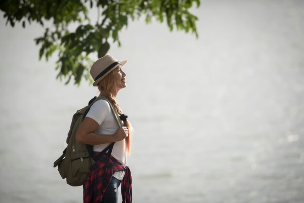 Jonge gelukkige vrouw met rugzak status die aan de rivier kijken.