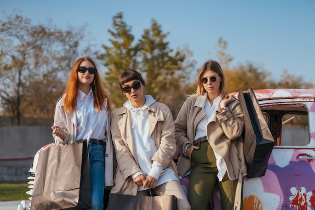 Jonge gelukkige vrouwen met boodschappentassen poseren in de buurt van een oude versierde auto