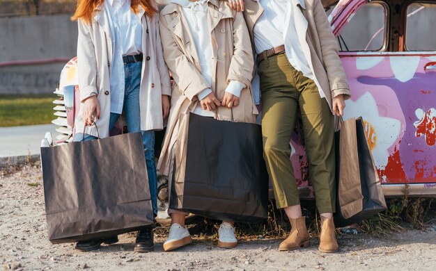 Jonge gelukkige vrouwen met boodschappentassen poseren in de buurt van een oude versierde auto