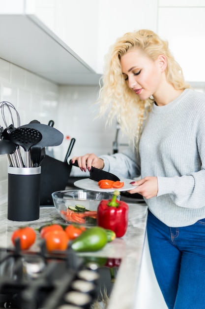 Gratis foto jonge gelukkige vrouwen scherpe tomaten voor binnen het maken van salade in de mooie keuken met groene verse ingrediënten. gezond eten en dieet concept.