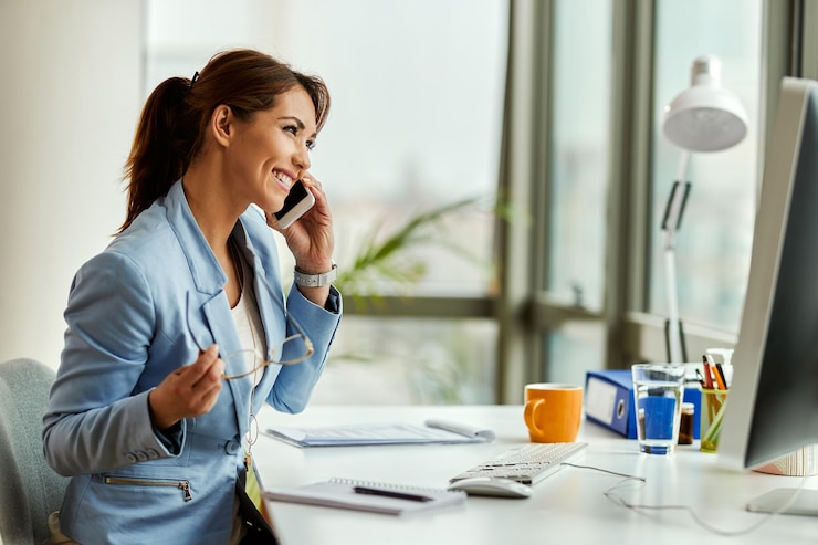 Gratis Foto jonge gelukkige zakenvrouw die mobiele telefoon gebruikt en op kantoor telefoneert
