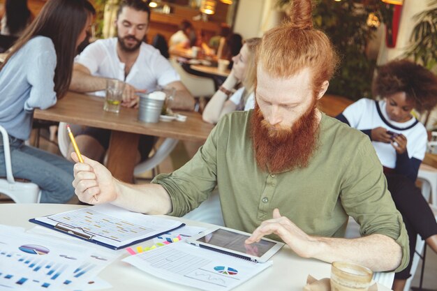 Jonge gember man met behulp van tablet in café